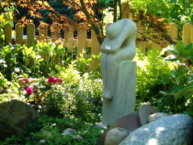 Gartenzaun im Hintergrund, bepflanzung und Skulptur davor